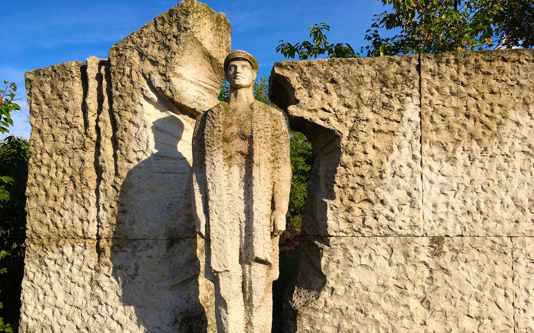 Statue of a soldier at Memento Park, Budapest, surrounded by textured stone.