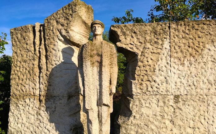 Statue of a soldier at Memento Park, Budapest, surrounded by textured stone.