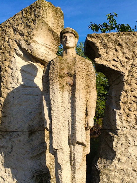 Statue of a soldier at Memento Park, Budapest, surrounded by textured stone.