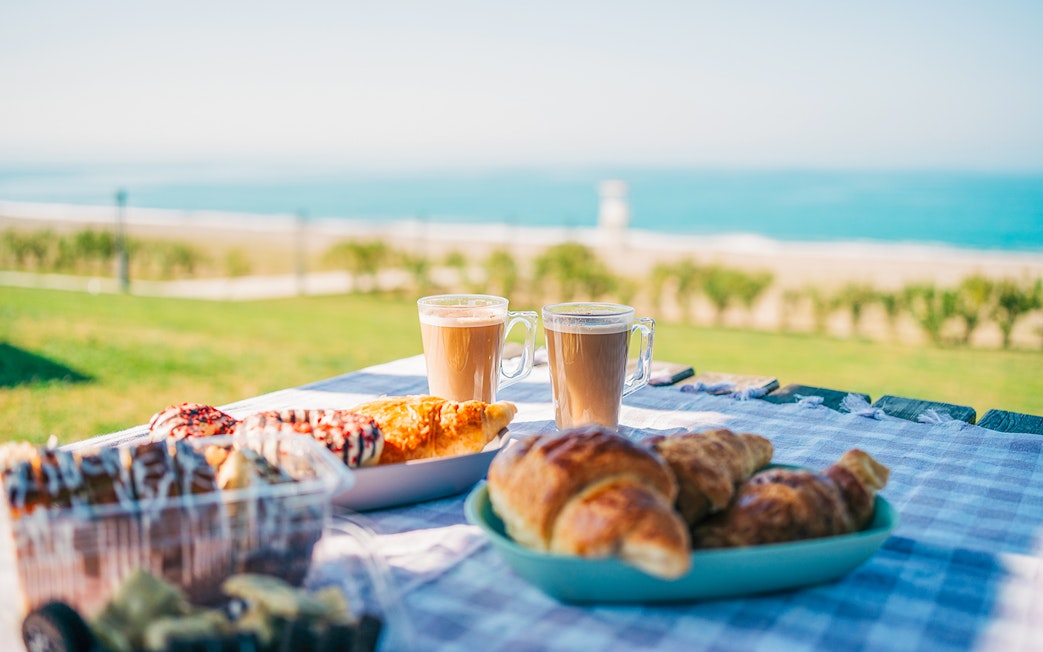 Breakfast with tea, coffee, and pastries on a table overlooking a beach.