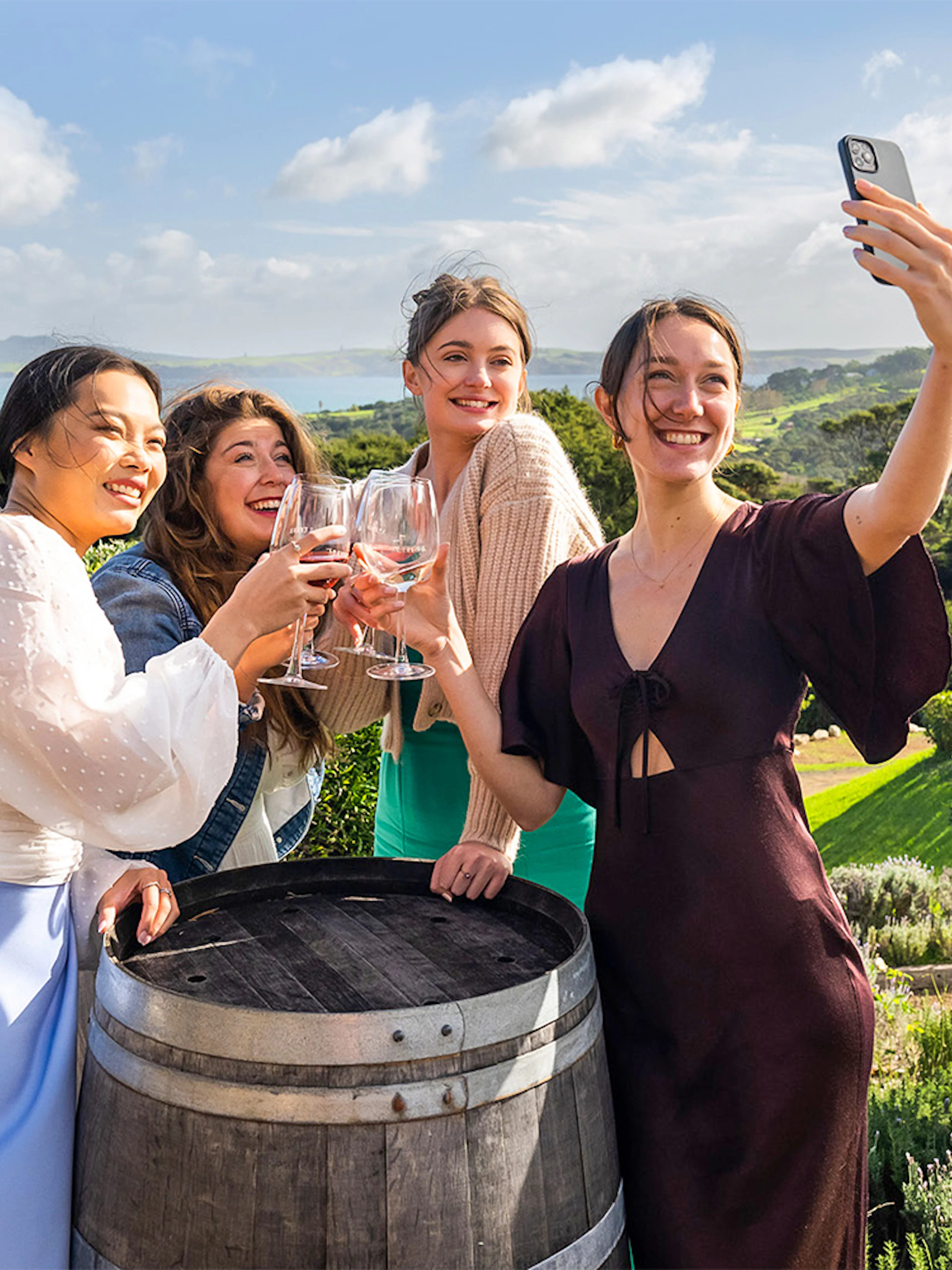 Women toasting with wine at Mudbrick Winery, Waiheke Island, with scenic vineyard view.