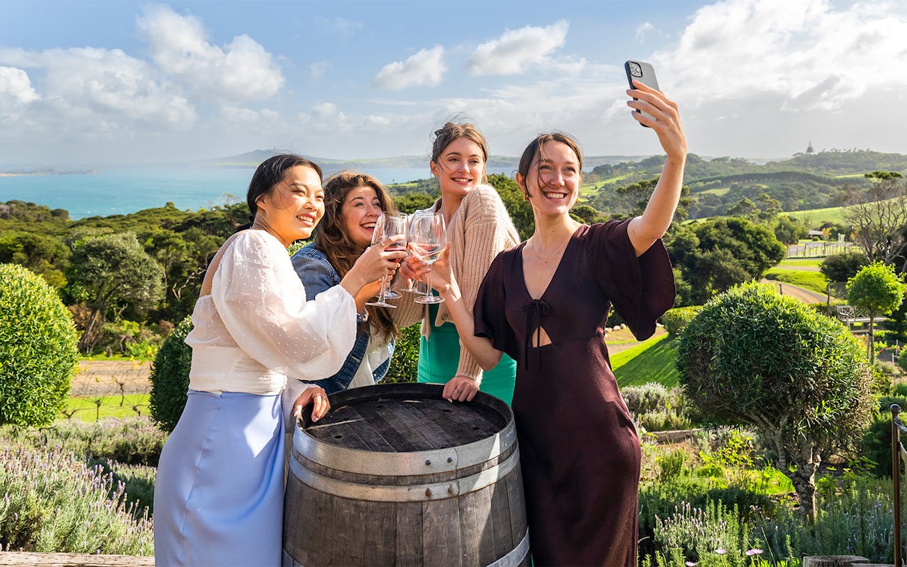 Women toasting with wine at Mudbrick Winery, Waiheke Island, with scenic vineyard view.