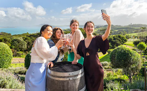 Women toasting with wine at Mudbrick Winery, Waiheke Island, with scenic vineyard view.
