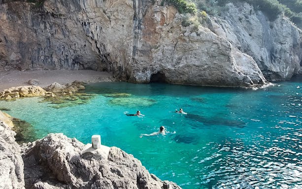 Swimmers in clear water near rocky cliffs at Betina Cave Beach.