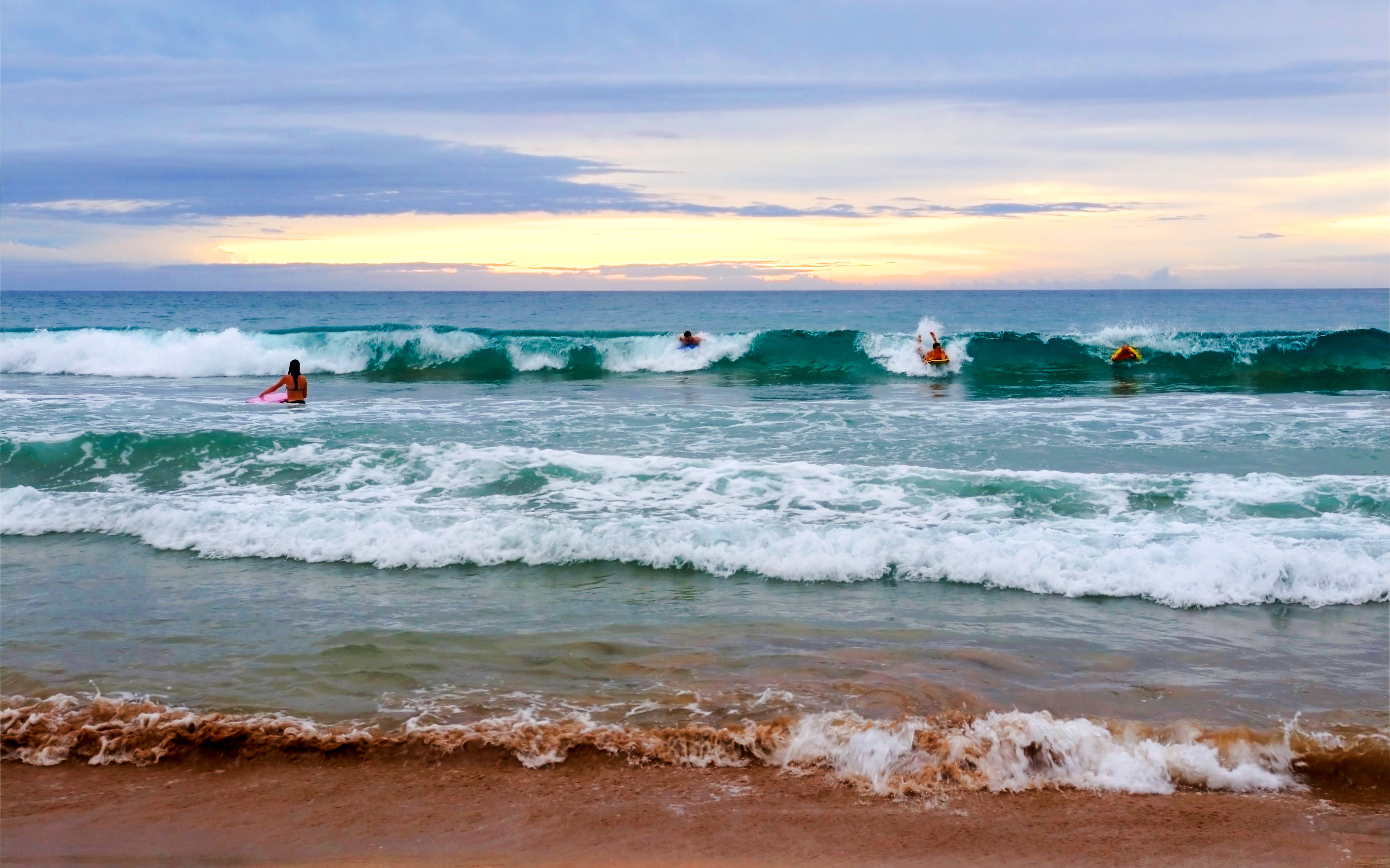 Surfers catching waves at Hapuna Beach during sunset.