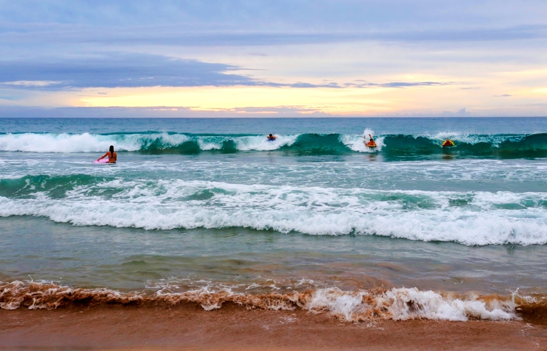 Surfers catching waves at Hapuna Beach during sunset.