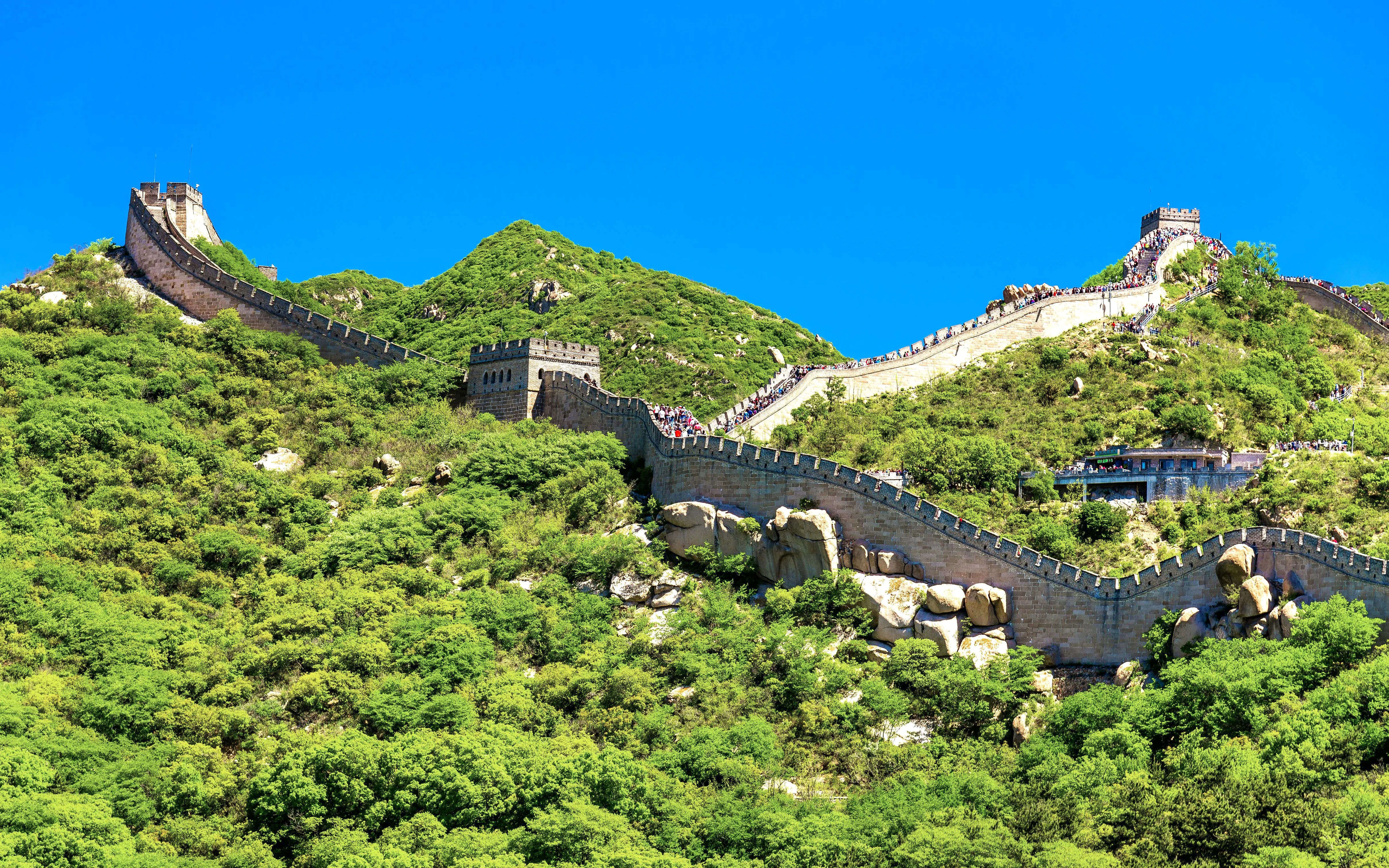 Great Wall of China winding over green hills under a clear blue sky.