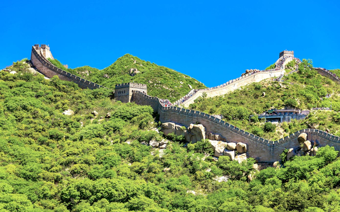 Great Wall of China winding over green hills under a clear blue sky.