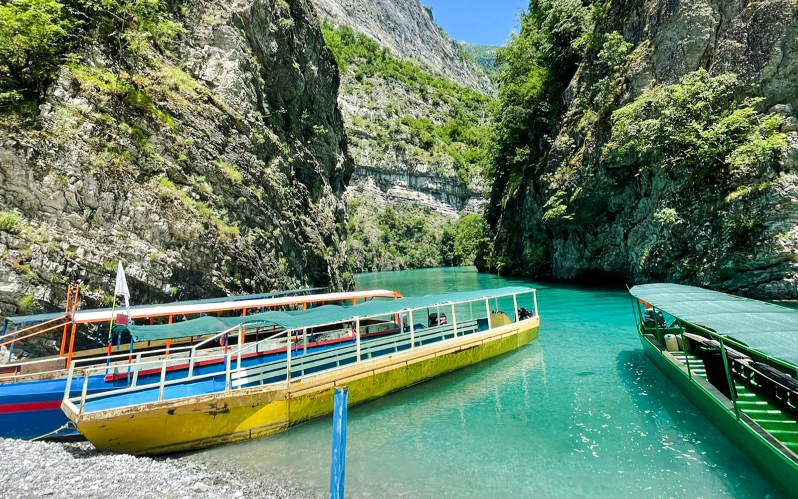 Boats docked at Shala River surrounded by rocky cliffs and clear water.