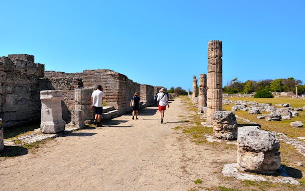 Visitors walking through ancient ruins at Paestum Archaeological Park, Italy.