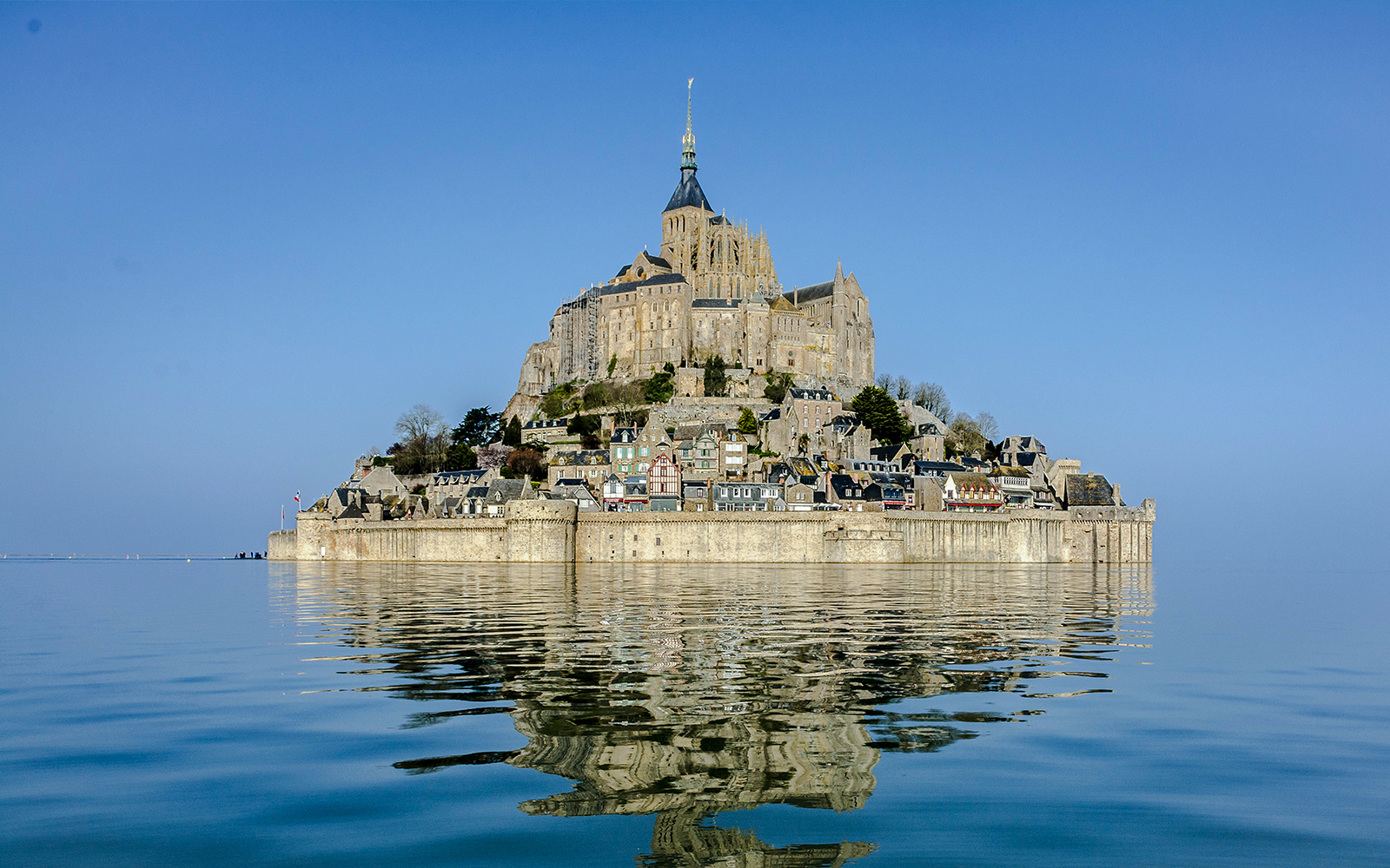 Mont Saint Michel reflected in calm water under a clear blue sky.