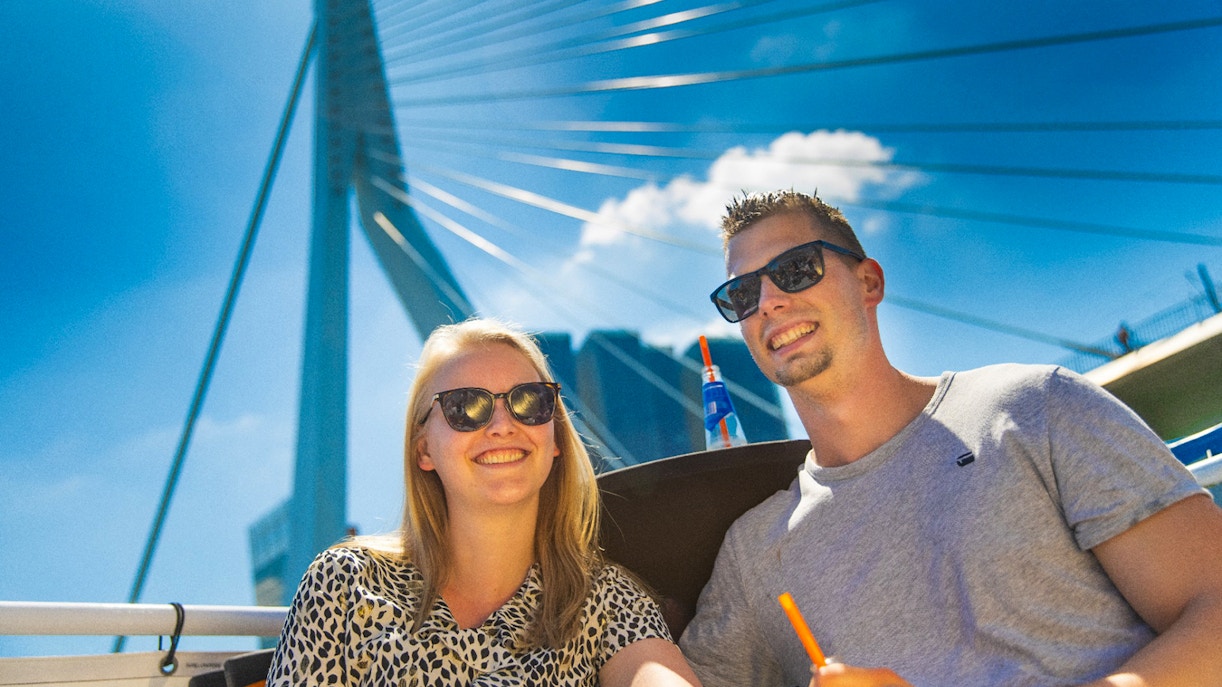 Guests enjoying a river cruise in Rotterdam with the Erasmus Bridge in the background.