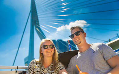 Guests enjoying a river cruise in Rotterdam with the Erasmus Bridge in the background.