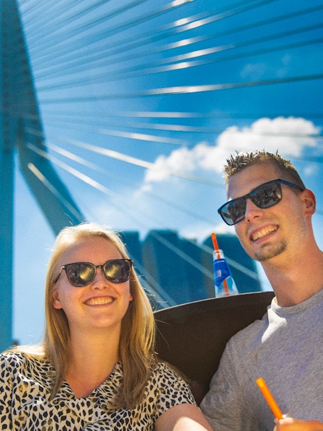 Guests enjoying a river cruise in Rotterdam with the Erasmus Bridge in the background.