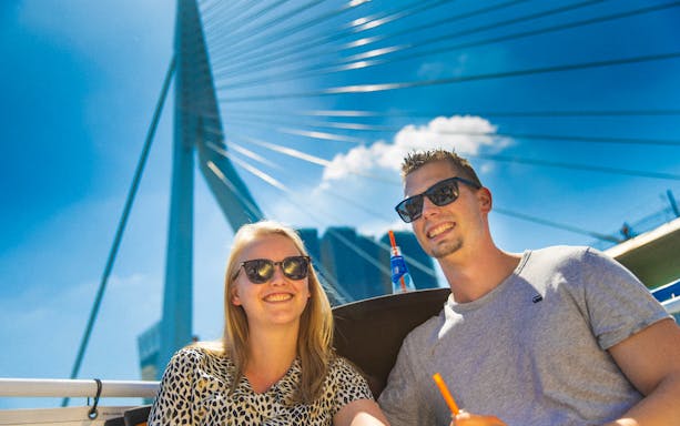 Guests enjoying a river cruise in Rotterdam with the Erasmus Bridge in the background.