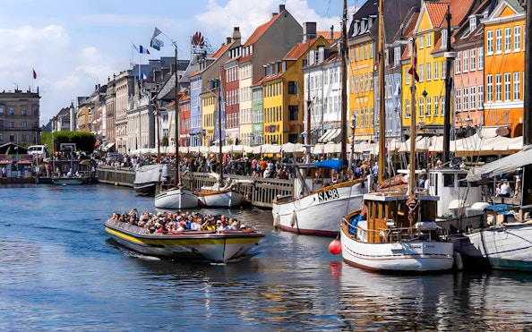 Tour boat navigating Nyhavn canal in Copenhagen with colorful buildings.
