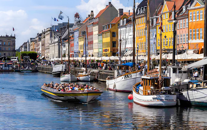 Tour boat navigating Nyhavn canal in Copenhagen with colorful buildings.