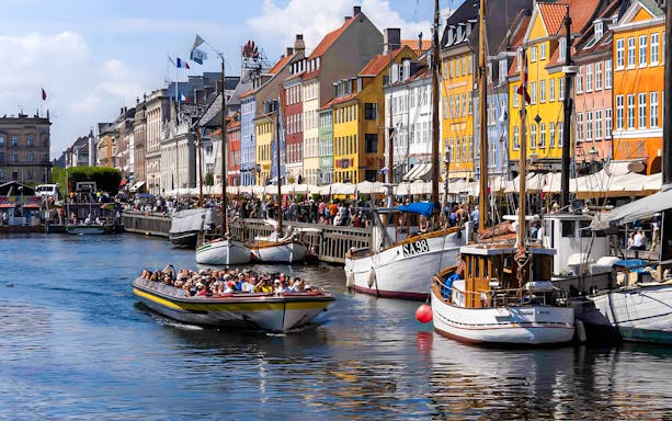 Tour boat navigating Nyhavn canal in Copenhagen with colorful buildings.