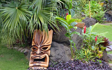 Tiki statue surrounded by tropical plants in the plantation garden at Luau Kalamaku.