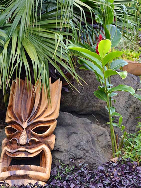 Tiki statue surrounded by tropical plants in the plantation garden at Luau Kalamaku.