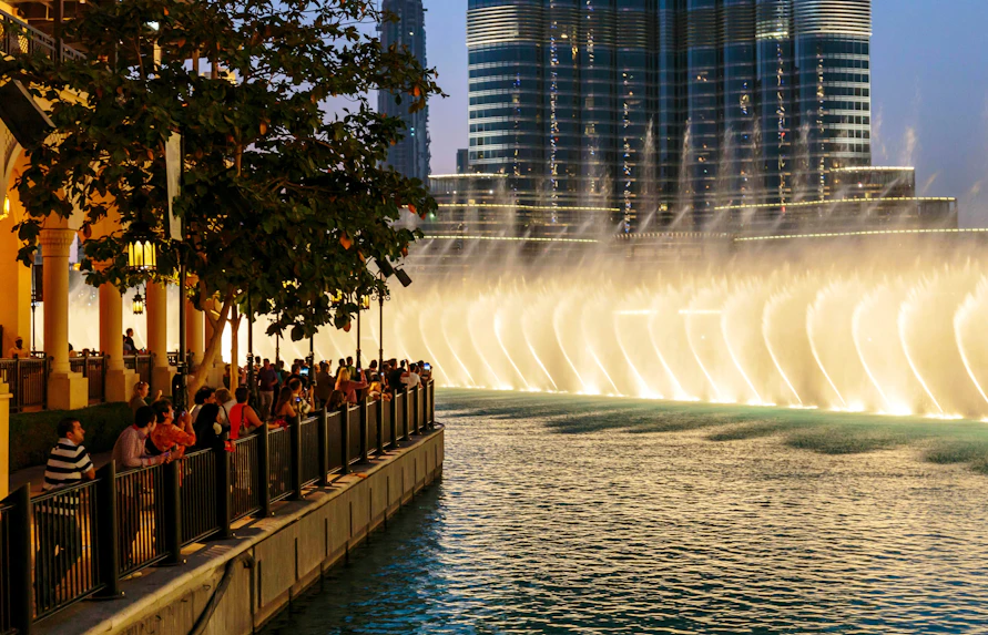 Crowd watching The Dubai Fountain show from the boardwalk with city skyline in the background.