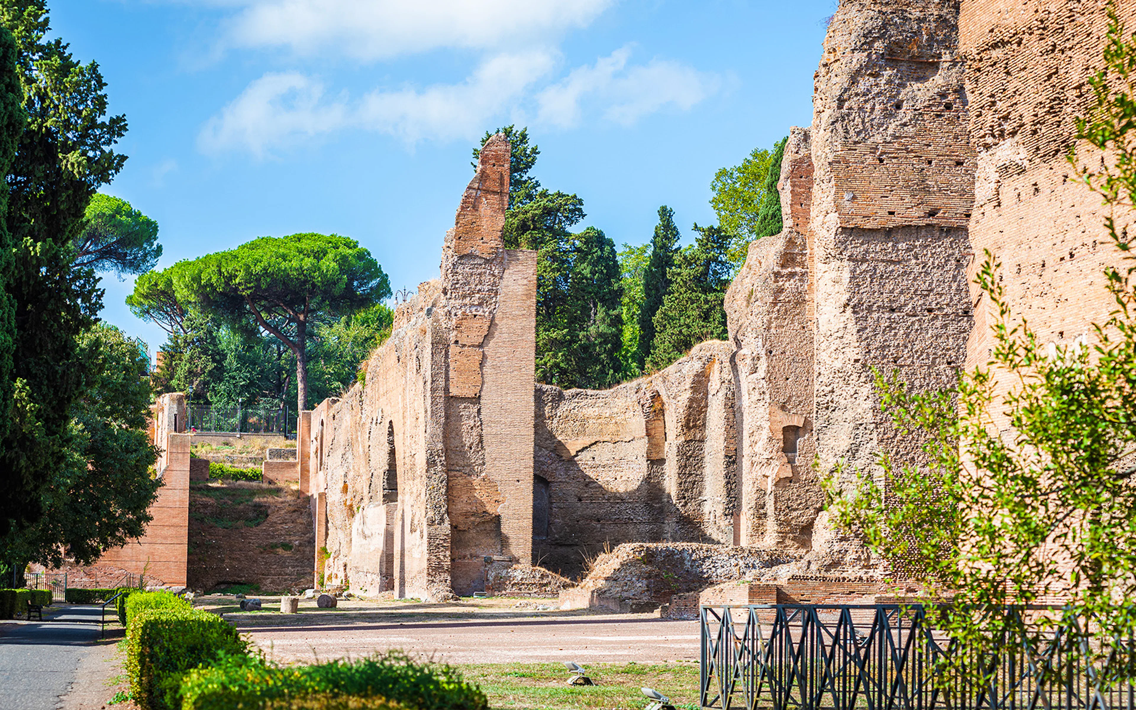 Ancient Roman ruins with brick walls and arches surrounded by trees, Italy.