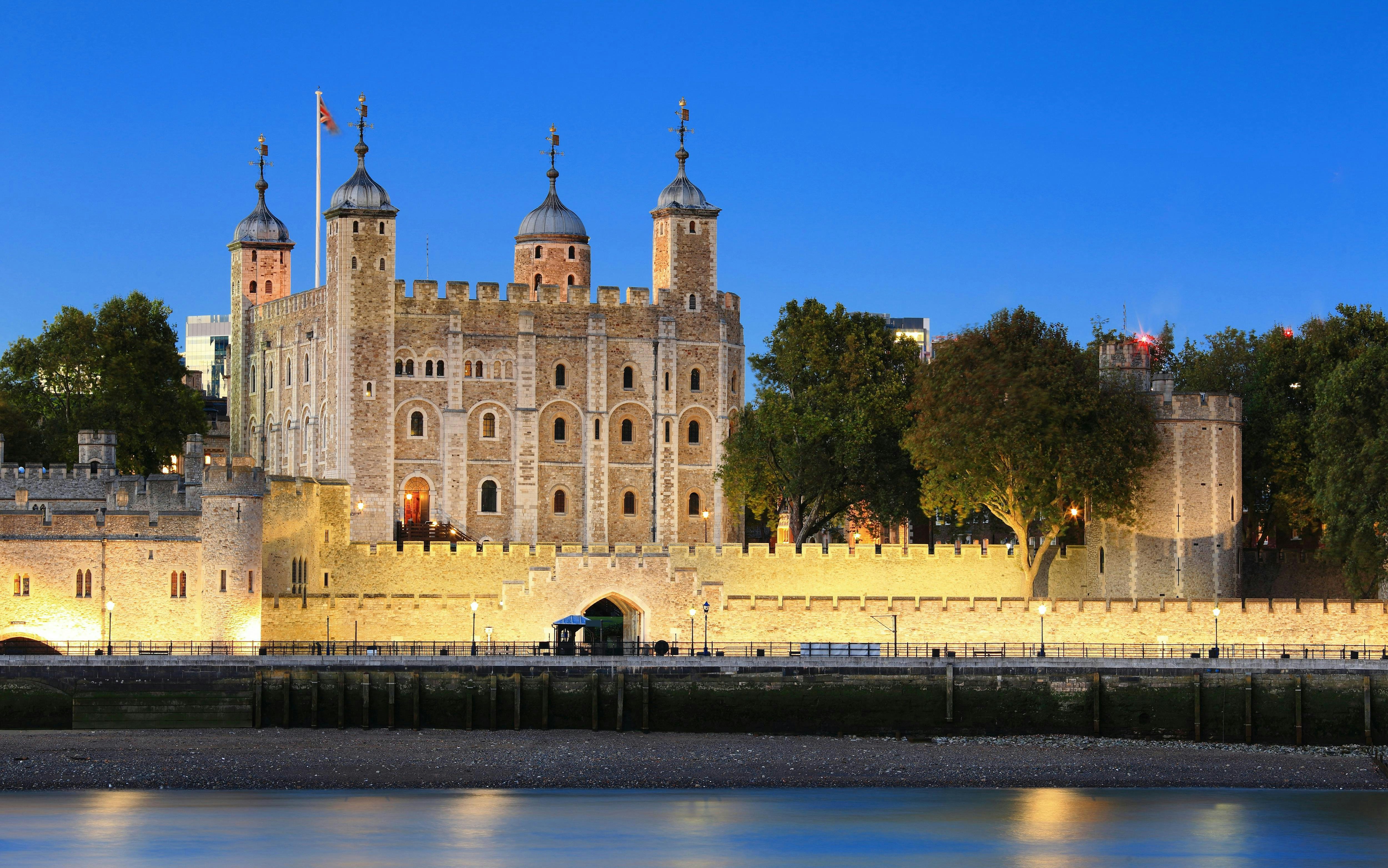 Tower of London illuminated at night, viewed from across the Thames River.