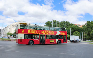 Big Bus tour on a street in Madrid, Spain, with city buildings and trees in the background.
