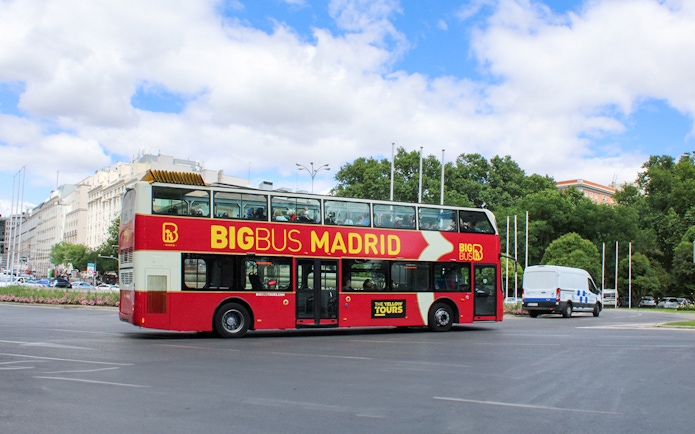 Big Bus tour on a street in Madrid, Spain, with city buildings and trees in the background.