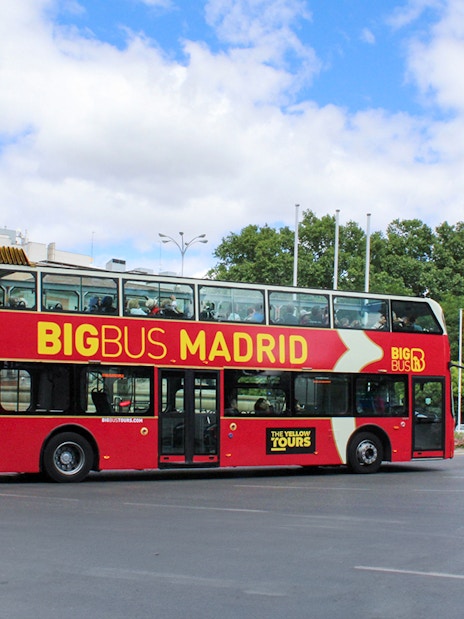 Big Bus tour on a street in Madrid, Spain, with city buildings and trees in the background.
