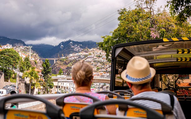 Hop-on hop-off bus tour in Funchal with view of cable cars and hillside houses.