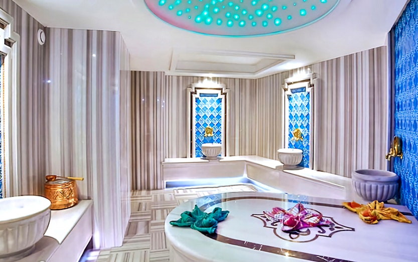 Private Turkish bath interior with marble benches, ornate blue tiles, and traditional basins.