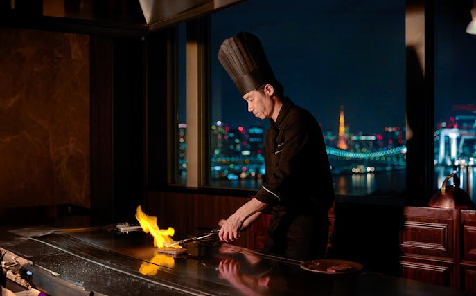 Chef grilling Kuroge Wagyu beef at Teppanyaki Ichou with city skyline view.