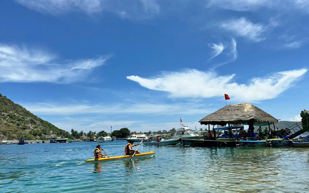 Kayakers in life vests paddle near a thatched-roof hut on Robinson Beach, Nha Trang.