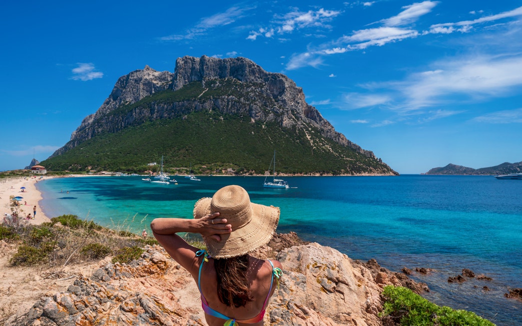 Girl in sun hat overlooking Tavolara Island beach and sea, Sardinia.
