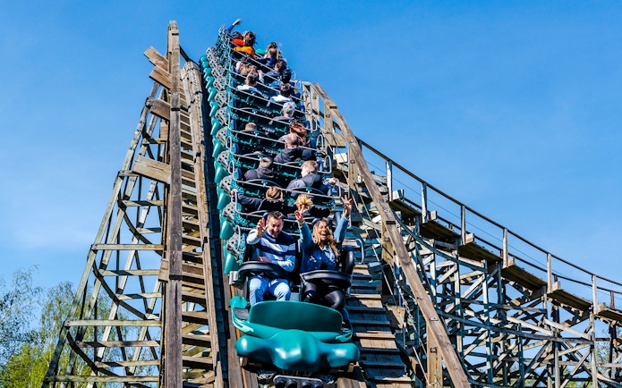 Roller coaster at Parc Asterix with riders descending a wooden track.