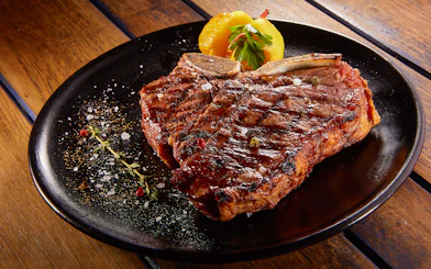 Grilled beef steak with rosemary on a black plate.