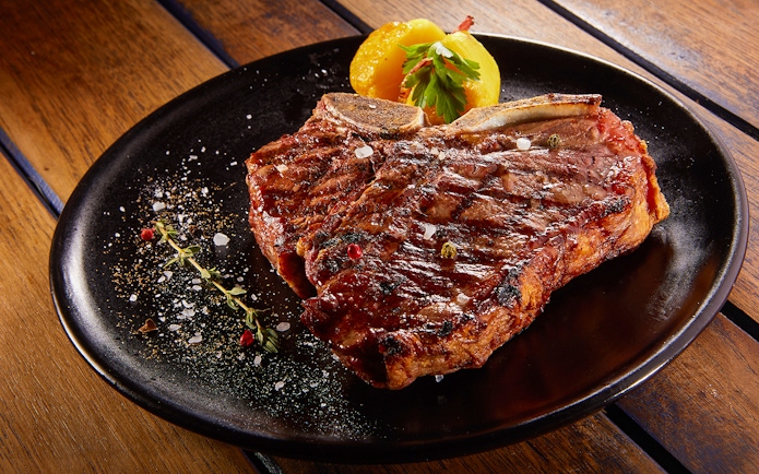 Grilled beef steak with rosemary on a black plate.