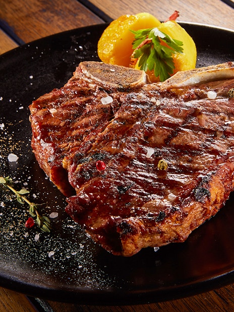 Grilled beef steak with rosemary on a black plate.