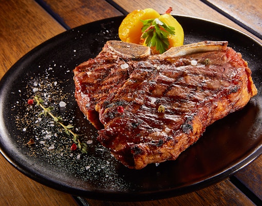 Grilled beef steak with rosemary on a black plate.