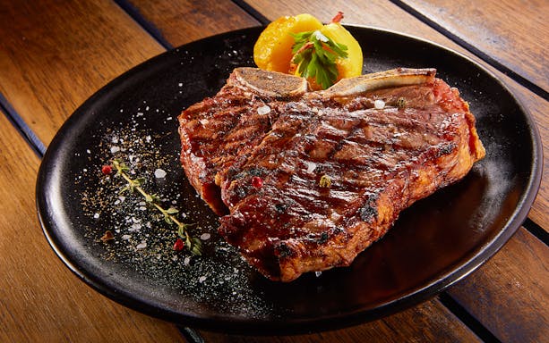 Grilled beef steak with rosemary on a black plate.