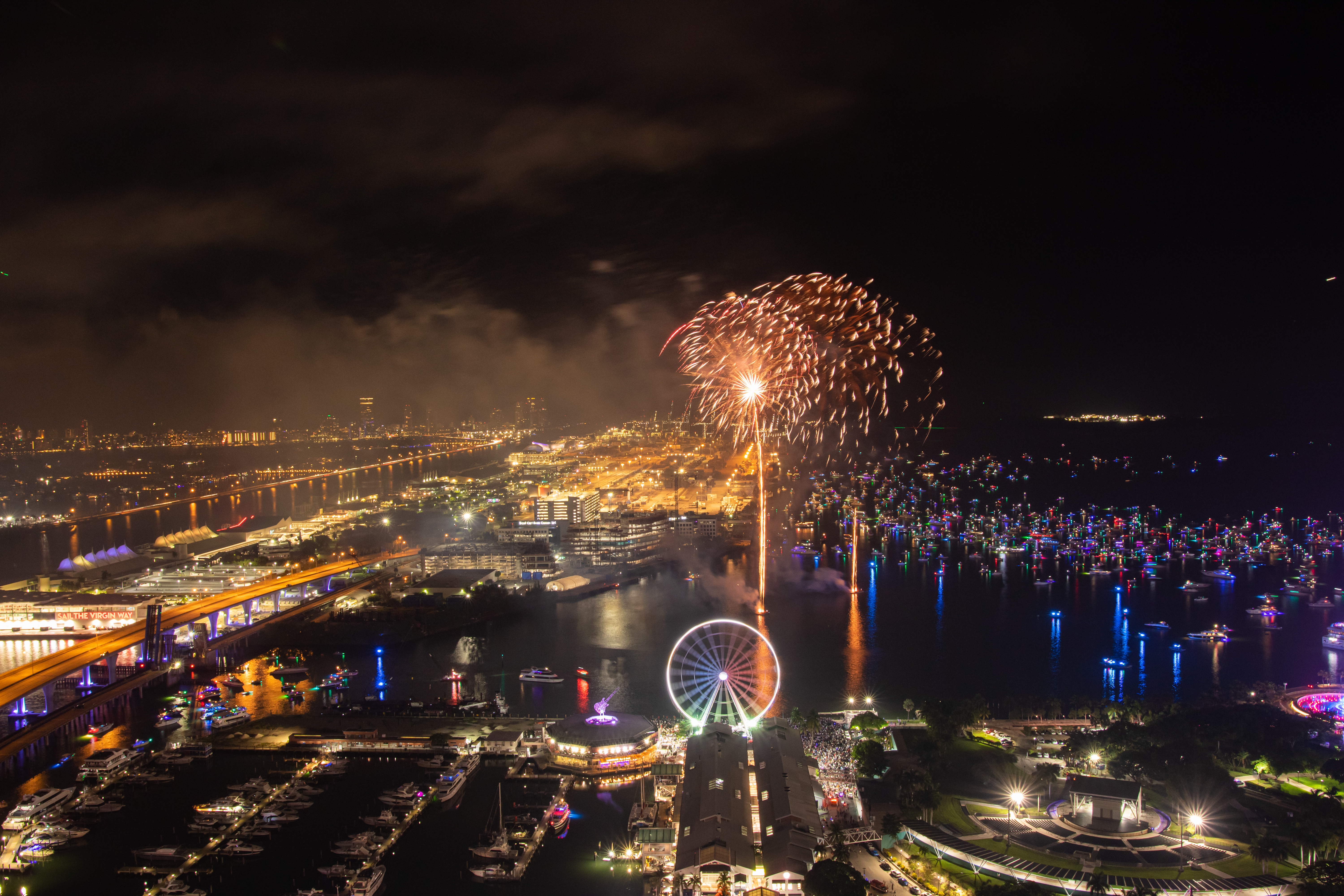 Fireworks over Bayfront Park and Marina in Miami at night with Ferris wheel and city lights.