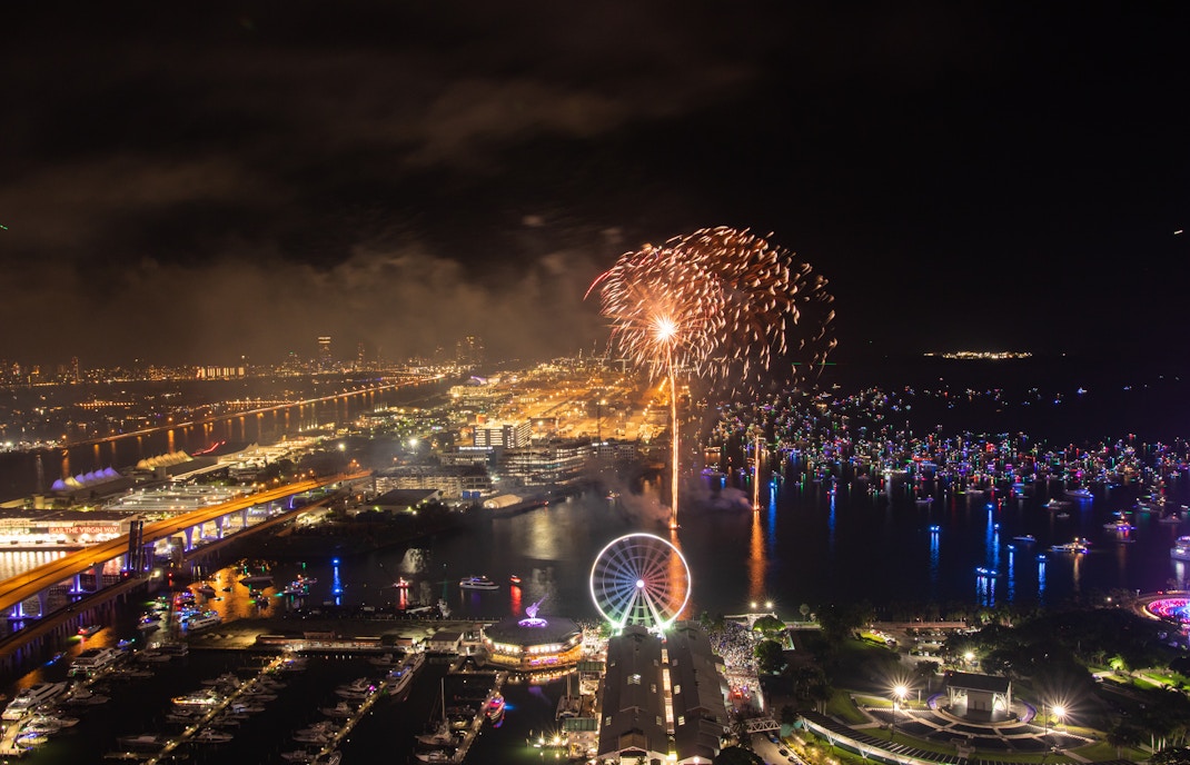 Fireworks over Bayfront Park and Marina in Miami at night with Ferris wheel and city lights.