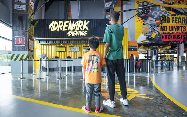 Father and child at Adrenark Adventure entrance, Dubai, holding hands.