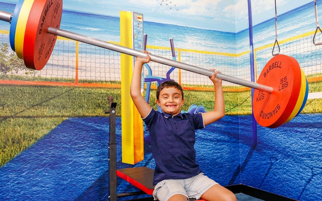 Child lifting oversized barbell in TRICKD: Illusions, Fun, & More exhibit.