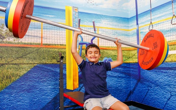 Child lifting oversized barbell in TRICKD: Illusions, Fun, & More exhibit.