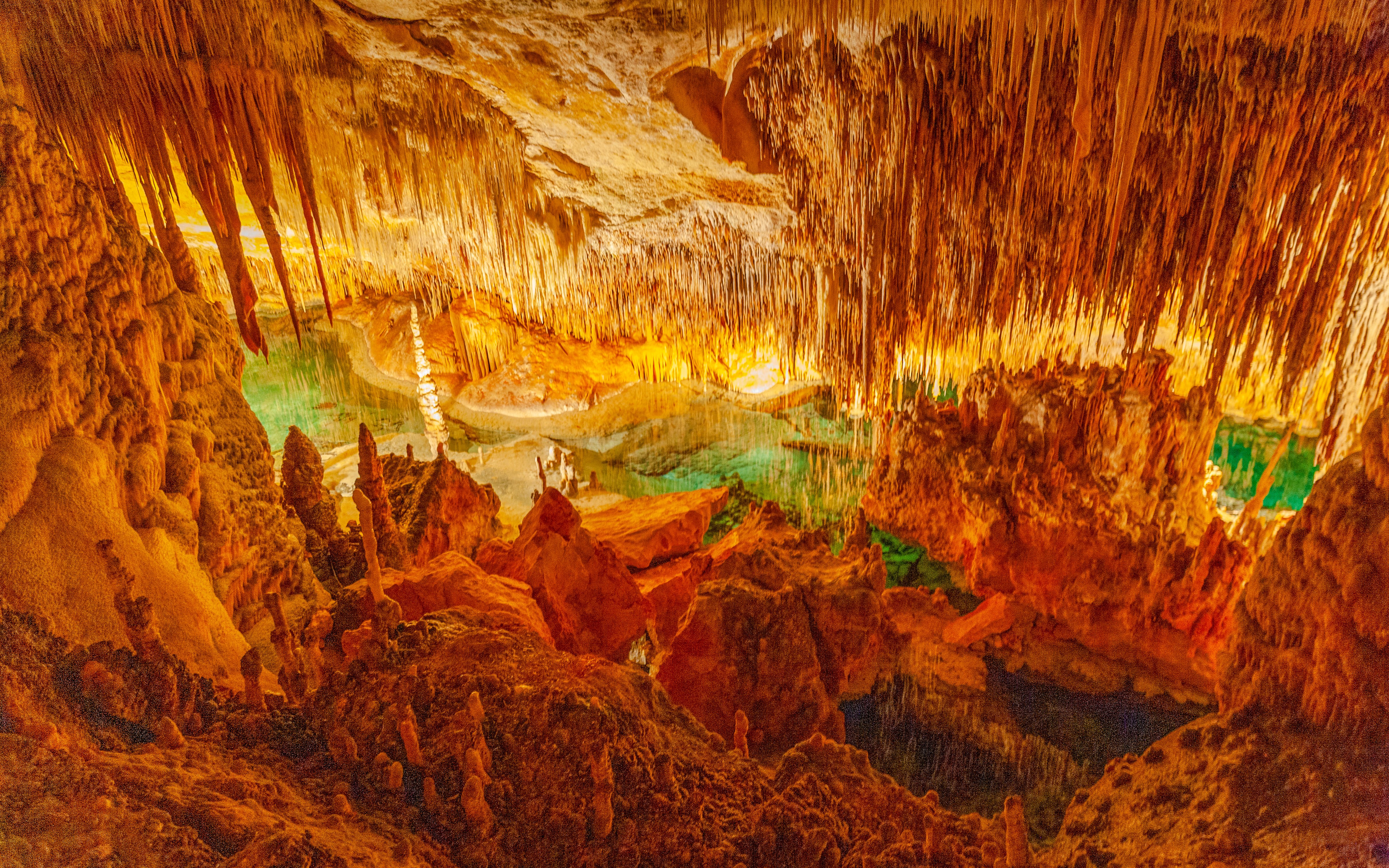 Stalactites and stalagmites in Drach Caves, Majorca, with illuminated rock formations and underground lake.