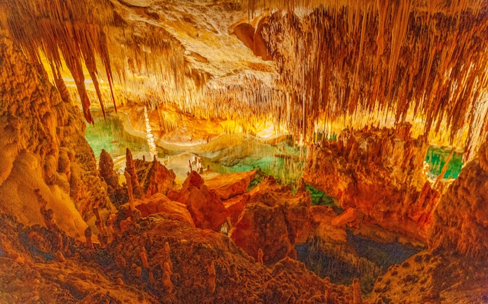 Stalactites and stalagmites in Drach Caves, Majorca, with illuminated rock formations and underground lake.