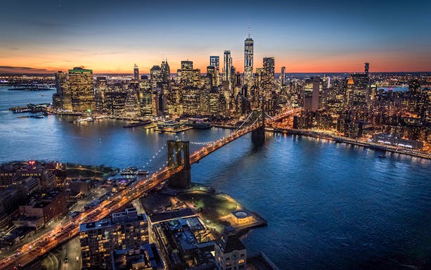 Brooklyn Bridge and Manhattan skyline at dusk during NYC helicopter night tour.