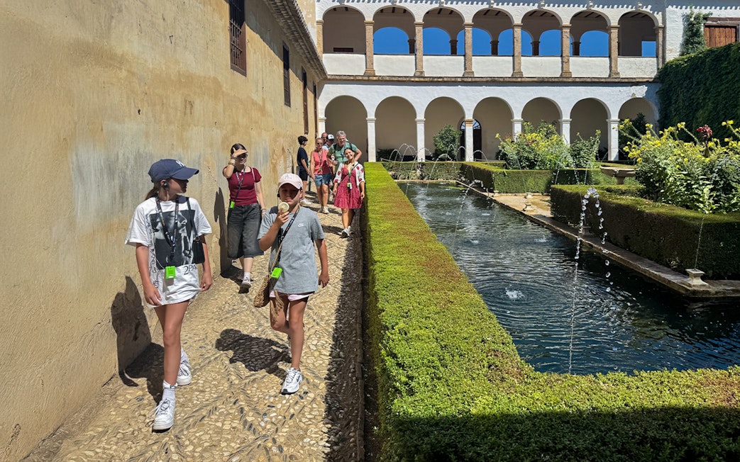 Tourists walking with guide at Alhambra courtyard, Granada, Spain.